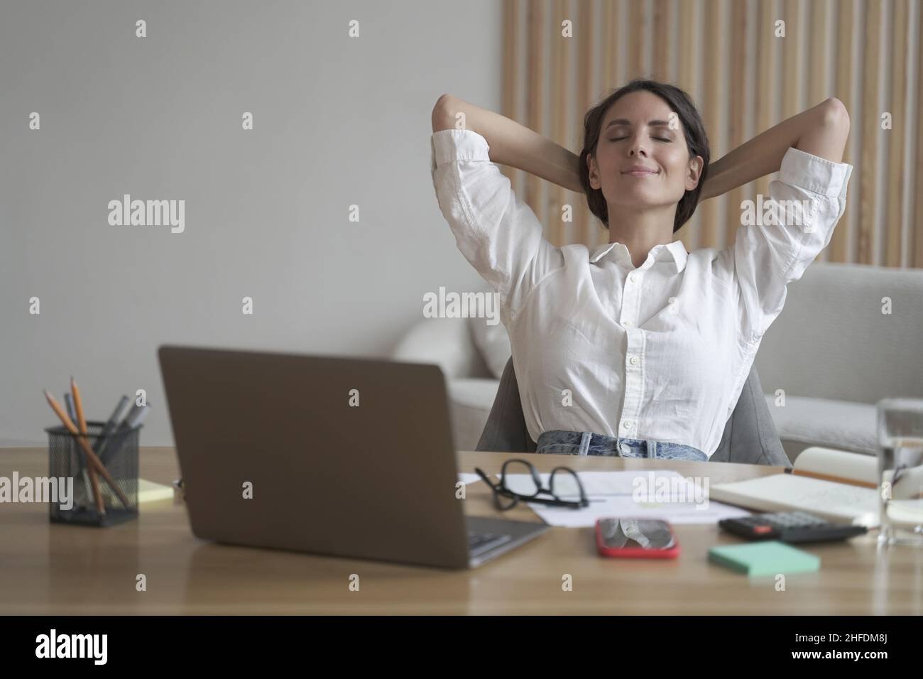 Young happy italian woman with hands behind head relaxing at workplace in home office Stock Photo