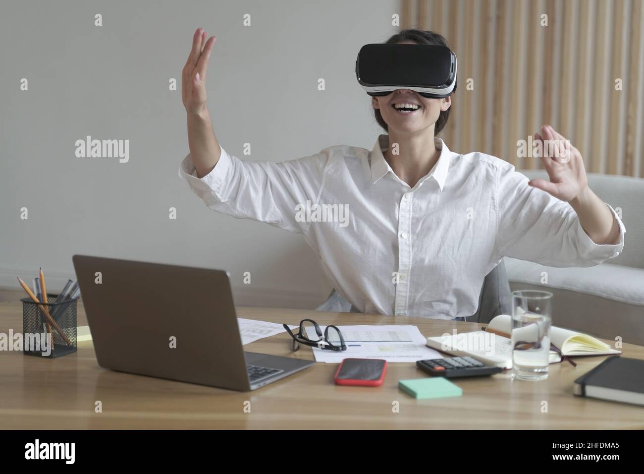 Joyful young business woman moving hands in air while using virtual reality glasses at workplace Stock Photo