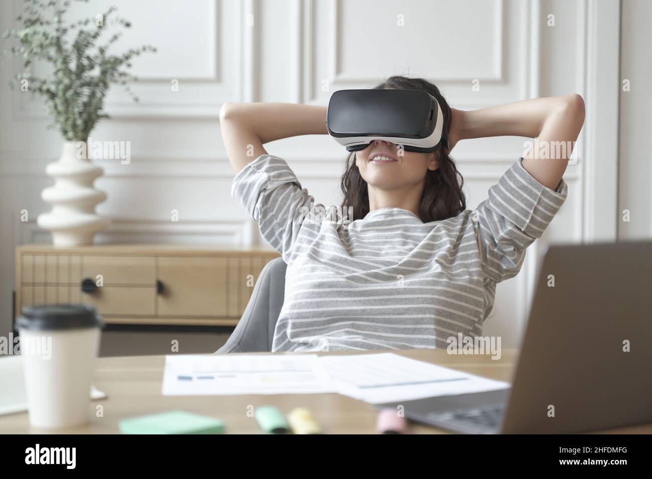 Relaxed young woman office worker in VR headset or helmet watching in 360 degrees video or movie Stock Photo