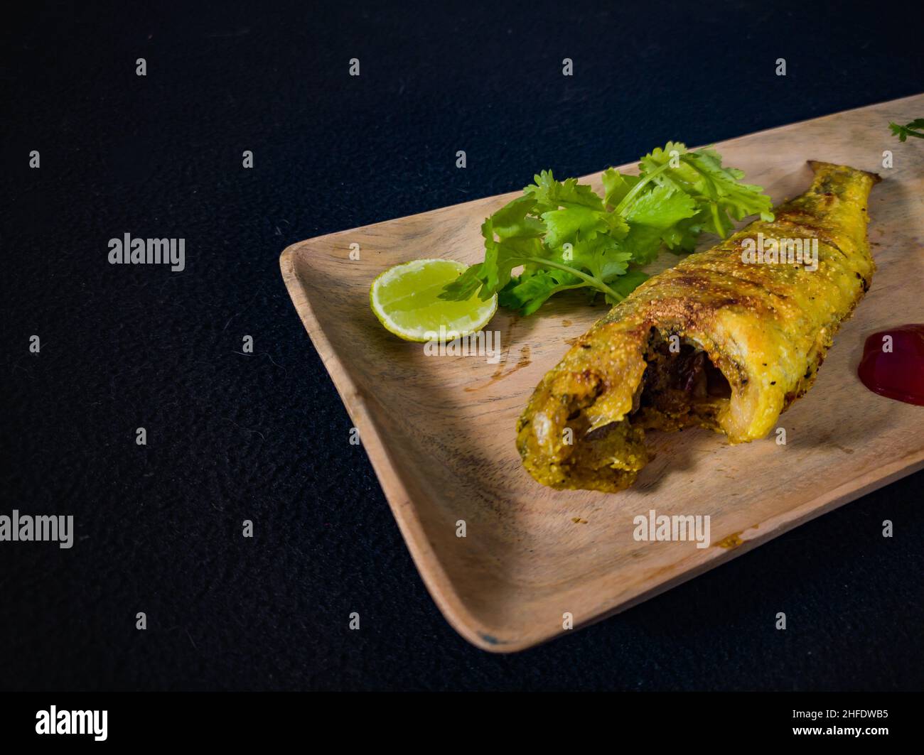 whole fish fry served on wooden plate garnished with lemon, coriander