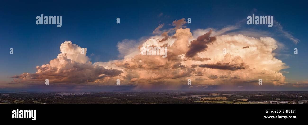 Frankston, Victoria, Australia, January 14, 2022: Aerial Panoramic of Powerful Thunder Head Storm Cloud Orange Against Blue Sky at Sunset Golden Hour Stock Photo