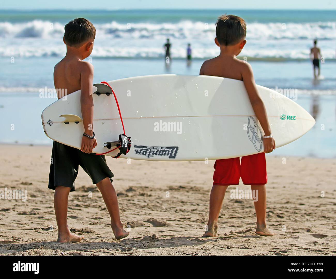 Two young Balinese boys carrying a surfboard at Kuta Beach, Bali in  Indonesia Stock Photo - Alamy
