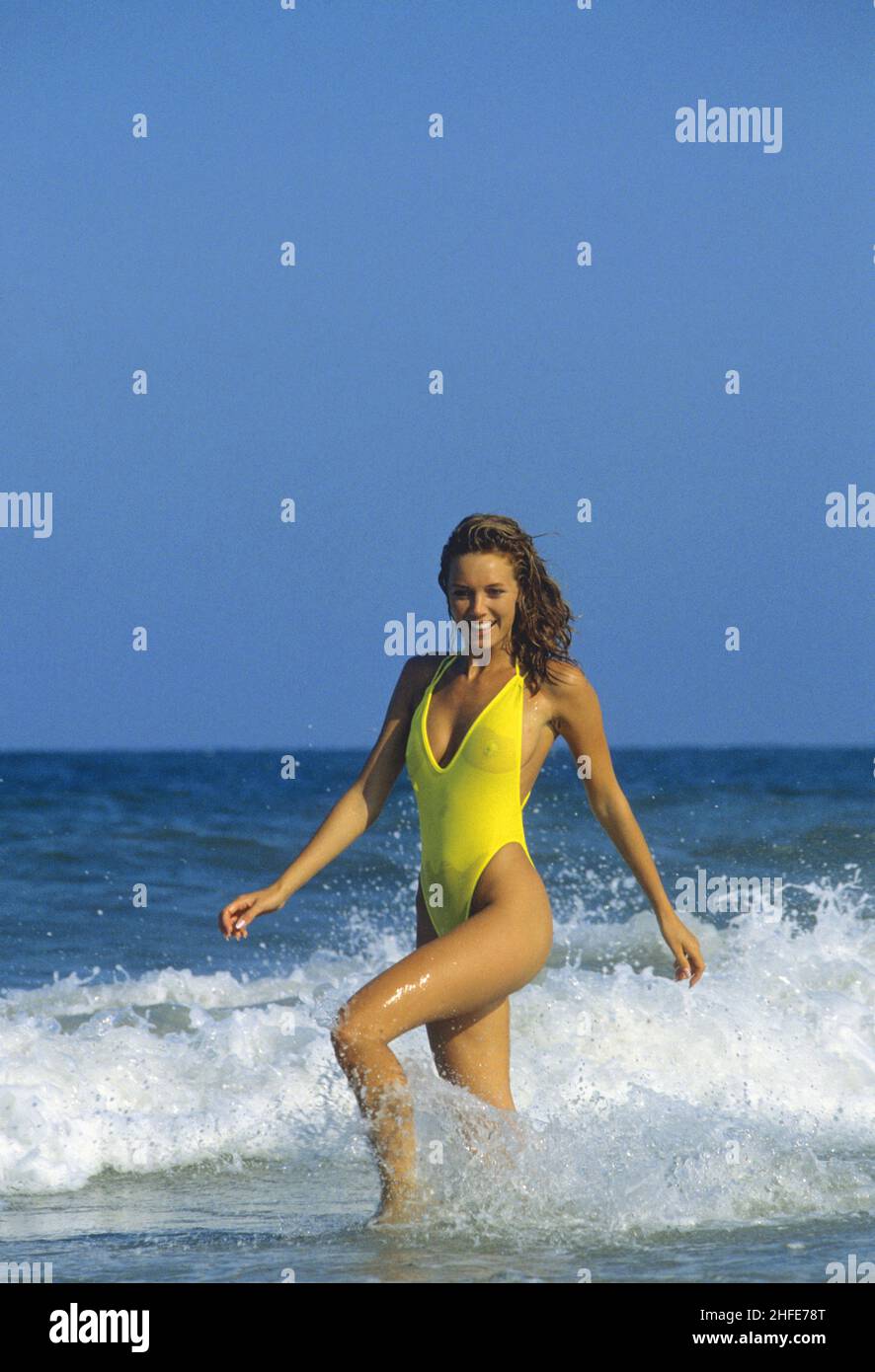 Pretty brown hair beauty happy looking playing waves gorgeous silhouette yellow bikini smiling in front camera blue sky and seawater on background Stock Photo