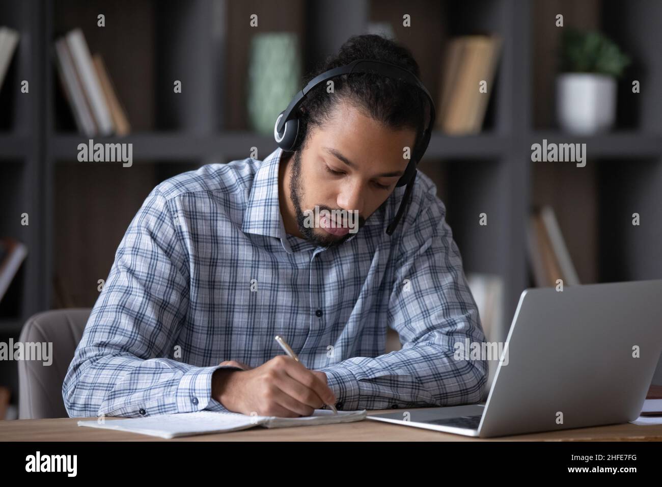 Focused student guy in headphones with mic writing notes Stock Photo