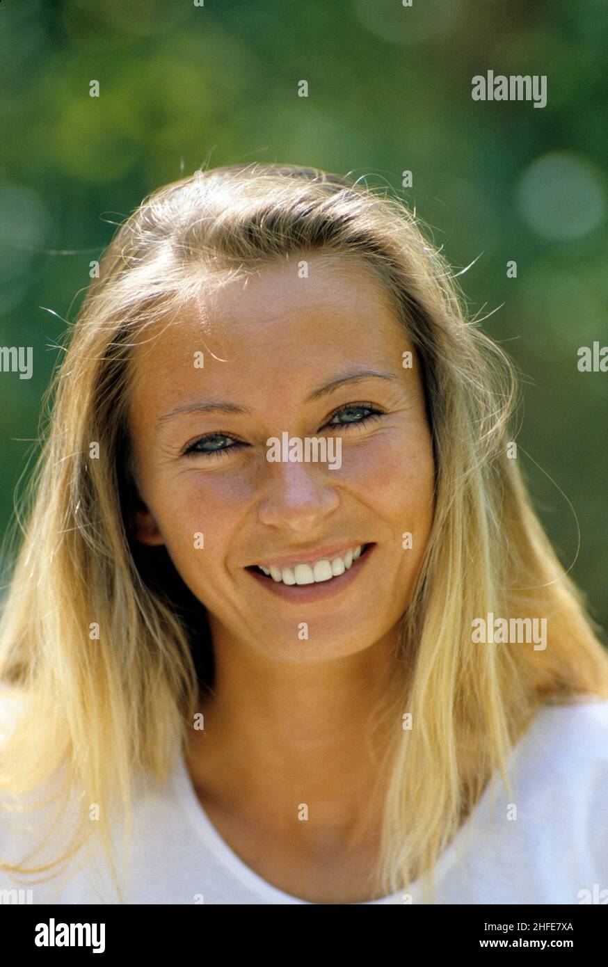 smiling and happy blond hair young woman portrait close up portrait profile looking  camera green foliage background natural light Stock Photo