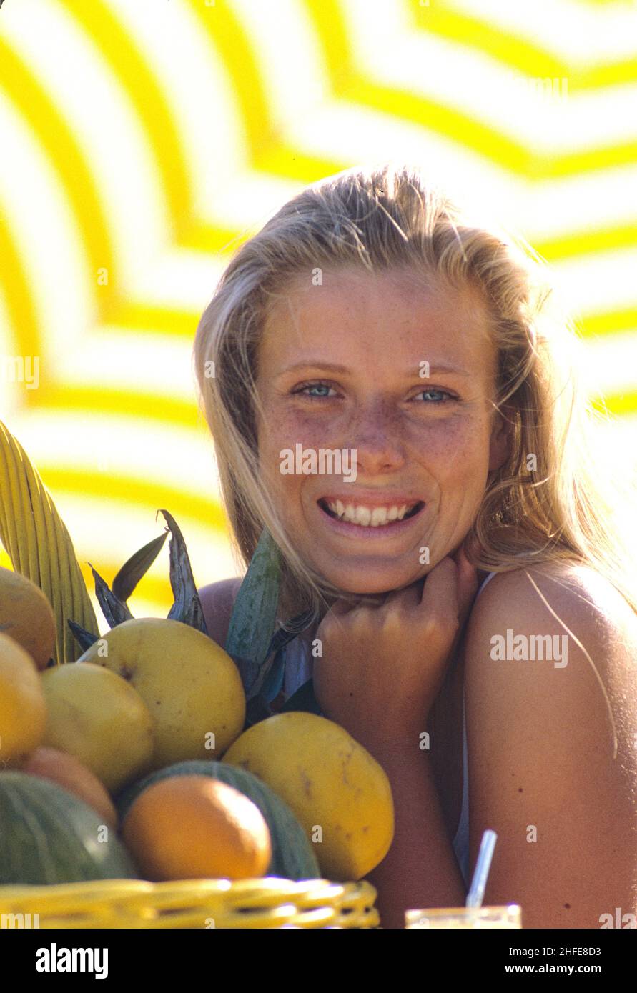 blond hair pretty young girl portrait sweet smiling face  blue eyes natural look above fruits basket yellow umbrella background Stock Photo