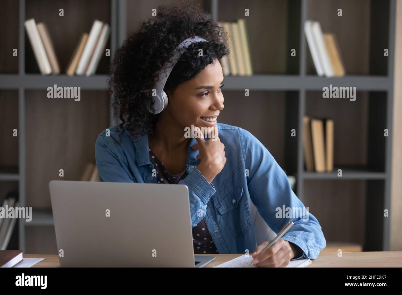 Thoughtful happy African student girl in wireless headphones listening ...