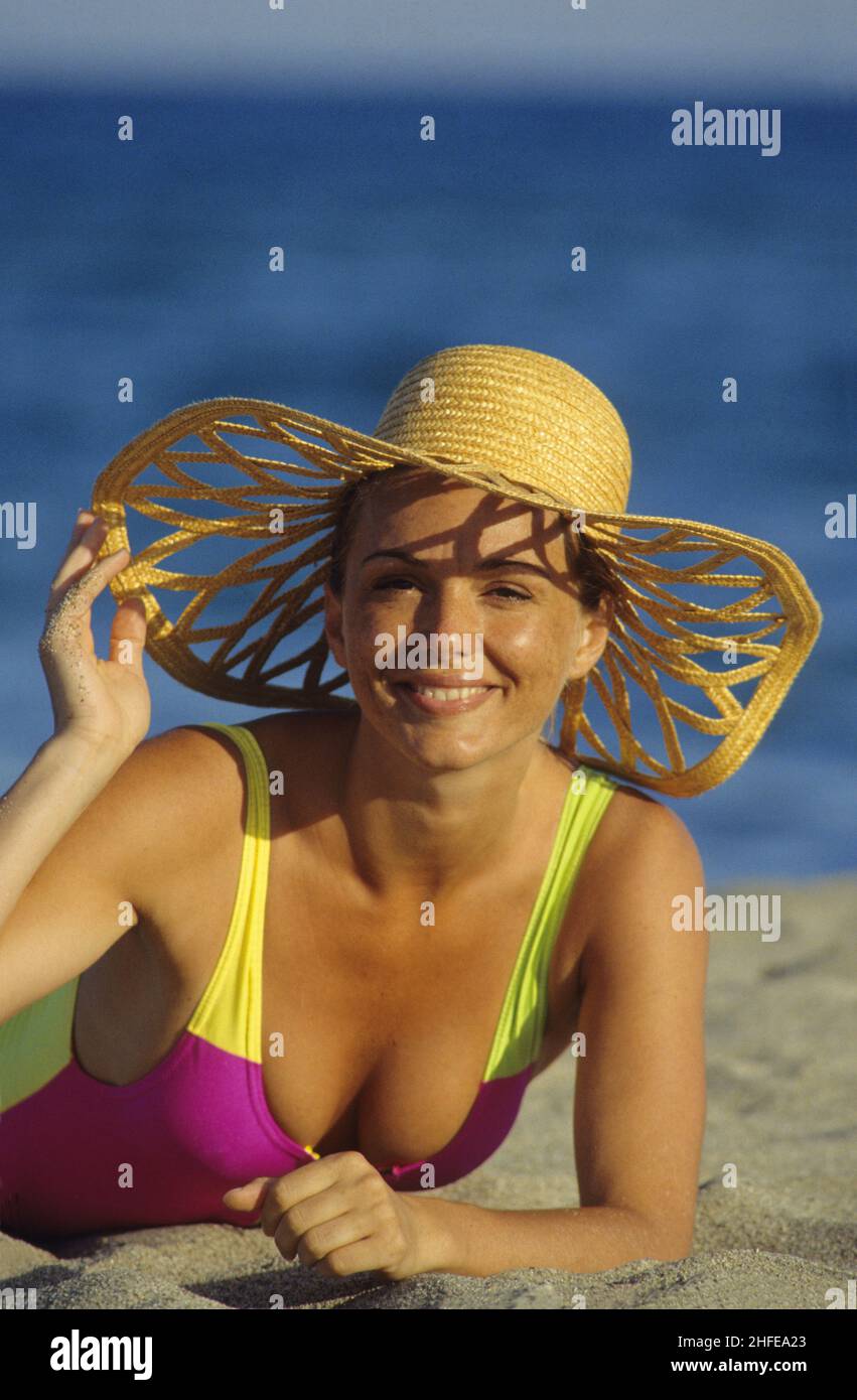 brown hair expressive smiling happy young woman portrait looking front camera with straw hat  blue sky seawater background Stock Photo