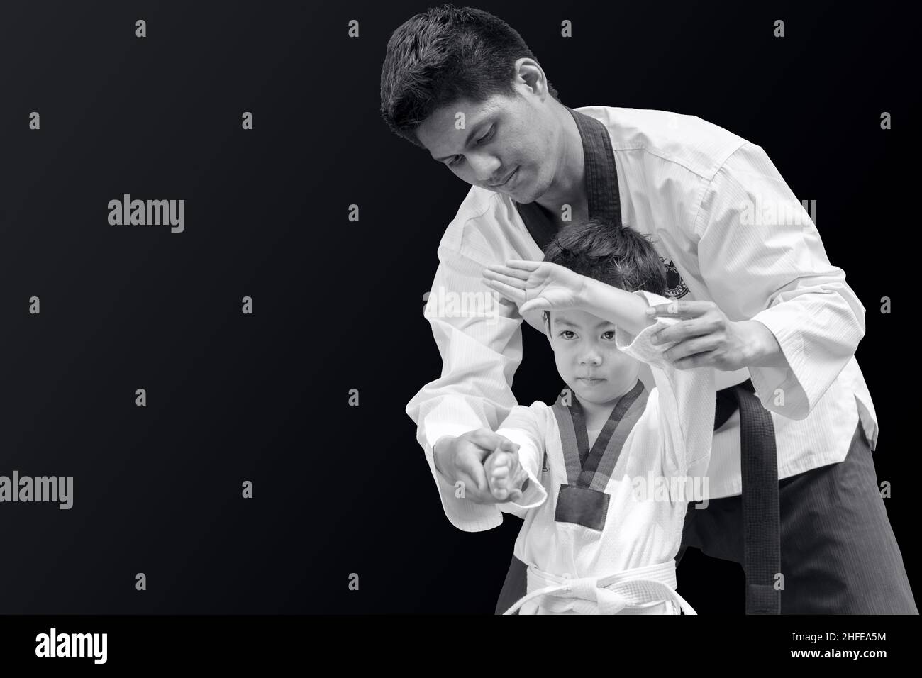 Taekwondo master black belt teaching kid to fight guard on black background Stock Photo