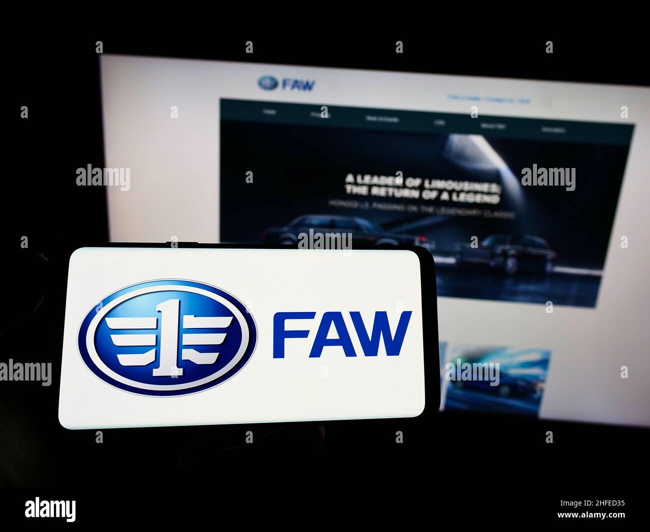 Person holding smartphone with logo of Chinese automotive company FAW Group Corporation on screen in front of website. Focus on phone display. Stock Photo