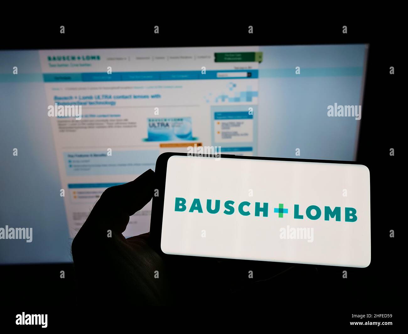 Person holding cellphone with logo of Canadian eye health company Bausch + Lomb on screen in front of business webpage. Focus on phone display. Stock Photo