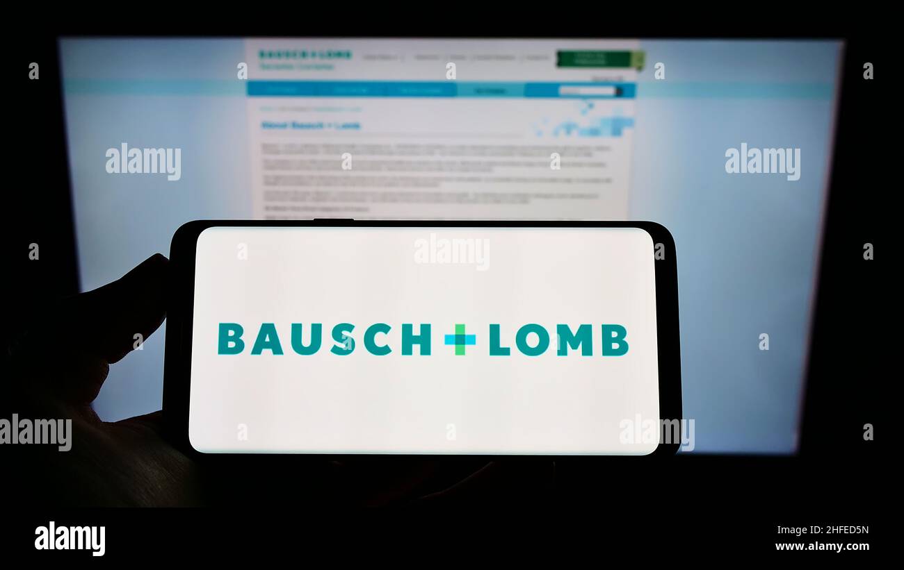 Person holding smartphone with logo of Canadian eye health company Bausch + Lomb on screen in front of business web page. Focus on phone display. Stock Photo