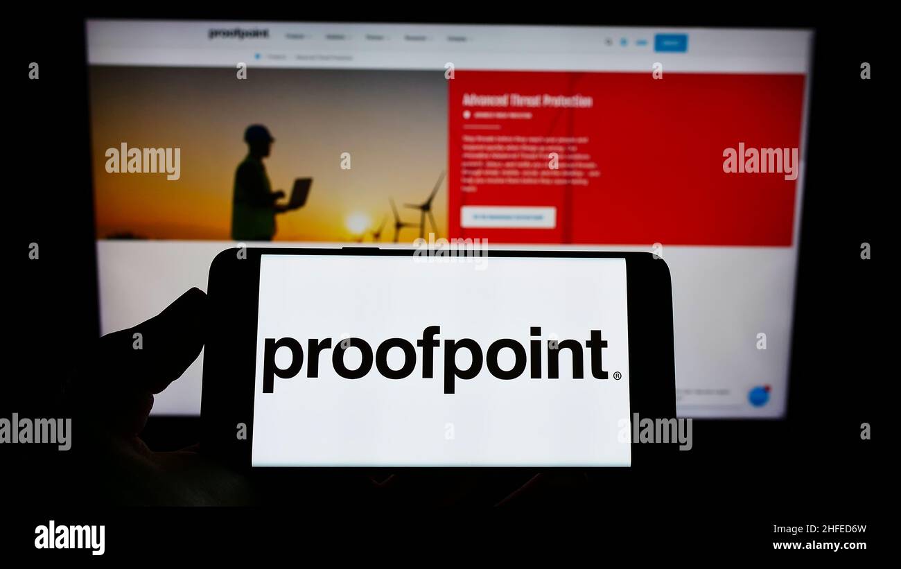 Person holding cellphone with logo of American security software company Proofpoint Inc. on screen in front of webpage. Focus on phone display. Stock Photo