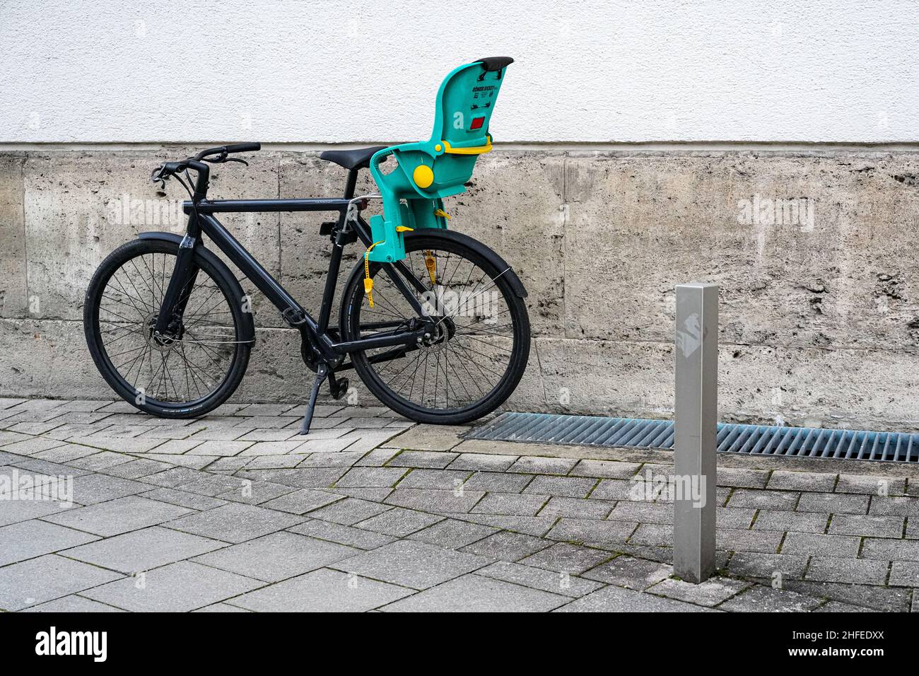 Black bicycle with green child seat on a sidewalk against a house wall. Stock Photo