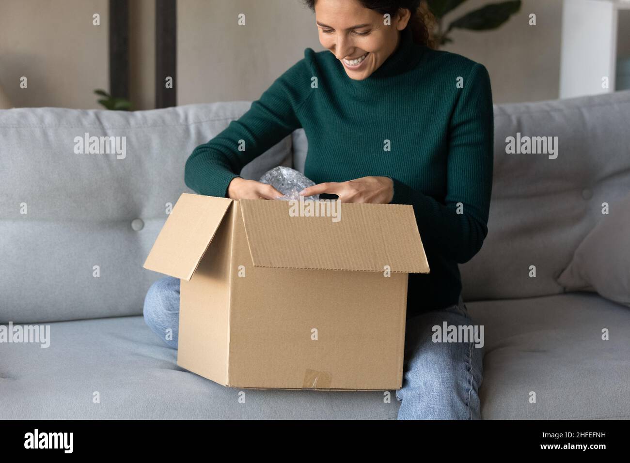 Happy millennial woman unpacking carton parcel at home. Stock Photo