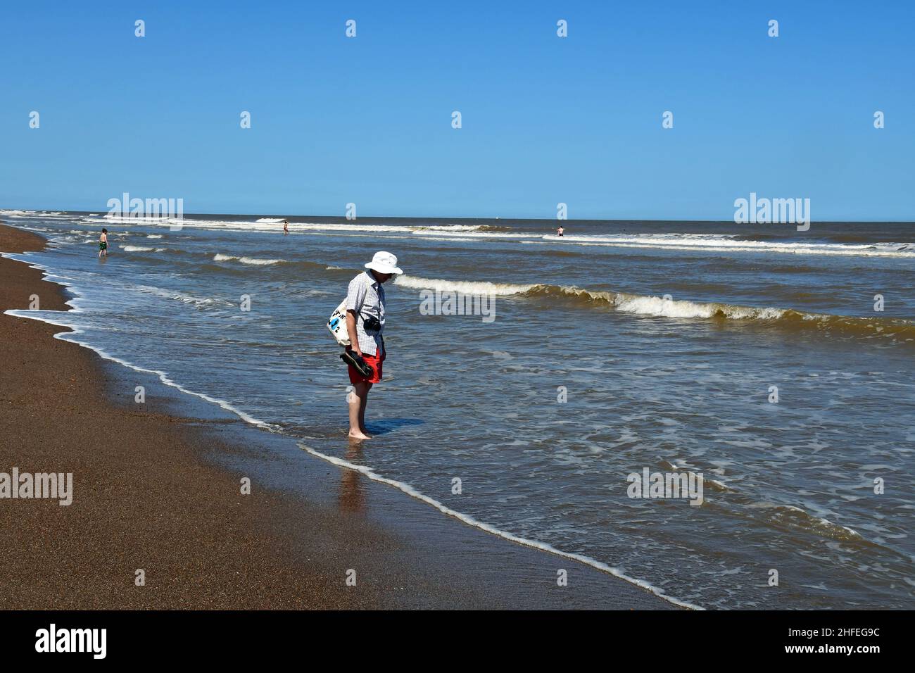 Man paddling in the sea at Chapel Six Marshes, Lincolnshire, UK Stock Photo