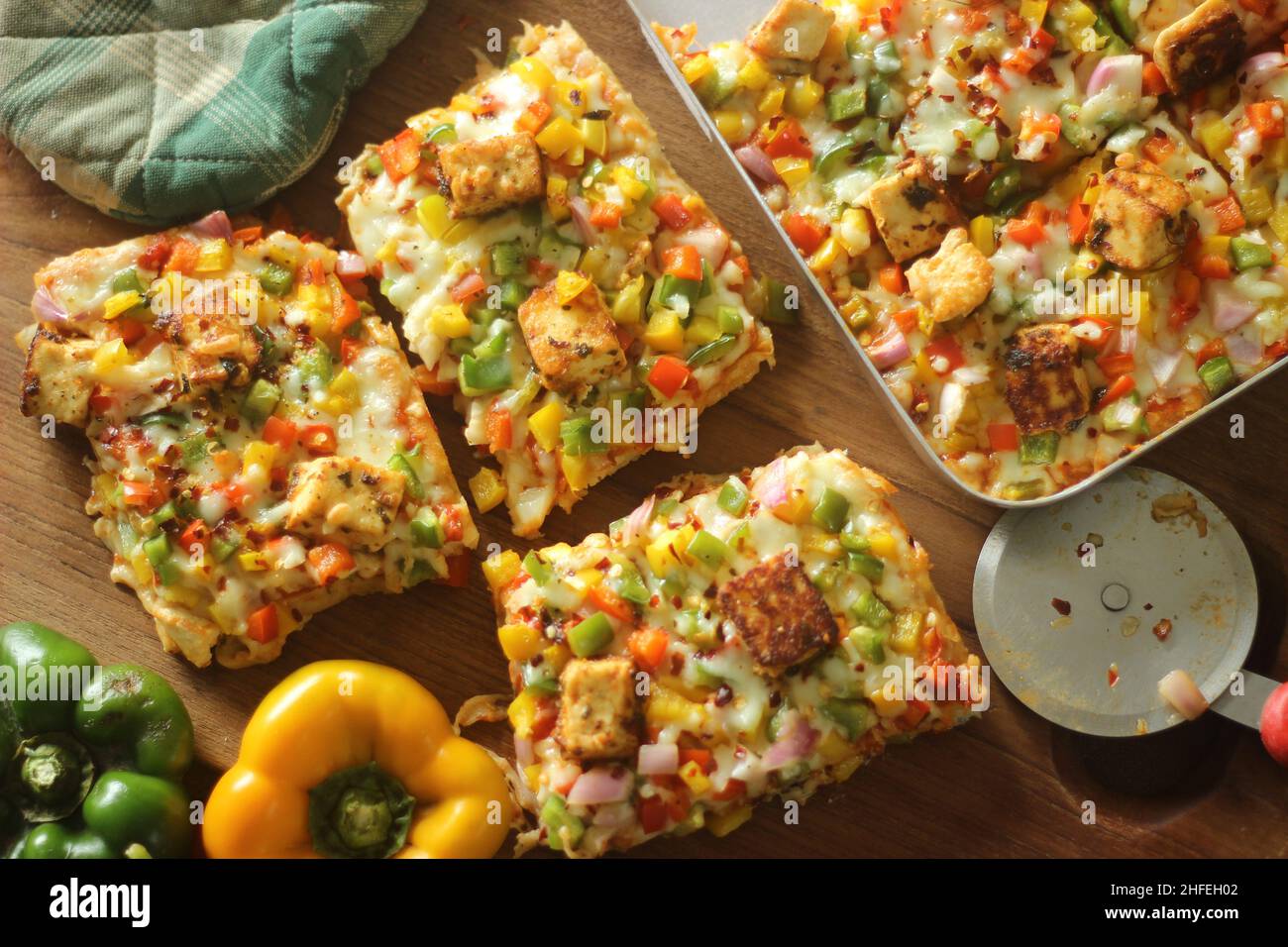 Rectangular slices of home baked pizza loaded with paneer, mozzarella cheese, red yellow green capsicums and onions. Baked in a rectangular tray Stock Photo