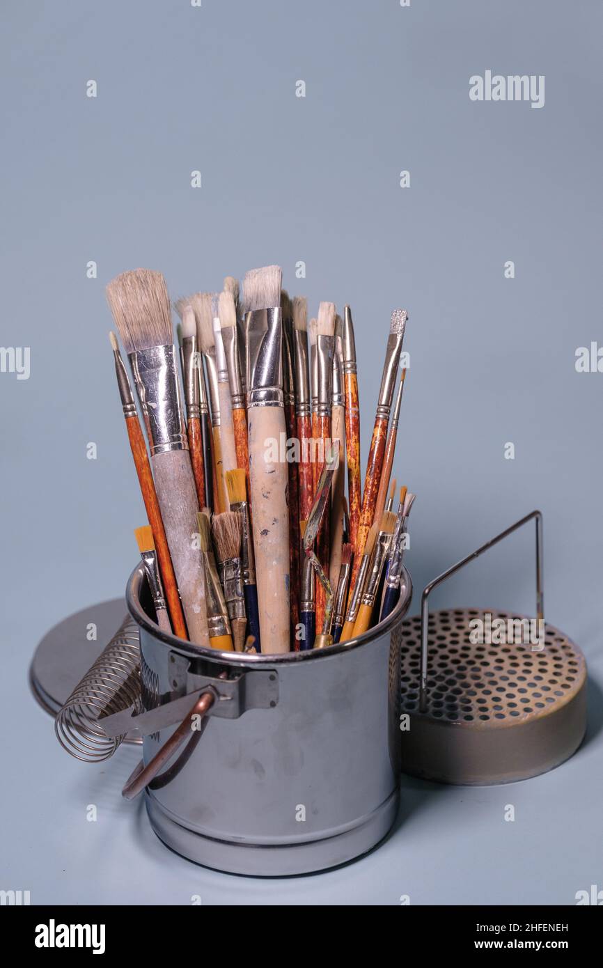 Tools of creativity - a bunch of grungy painter's brushes in a metal bucket on blue background Stock Photo