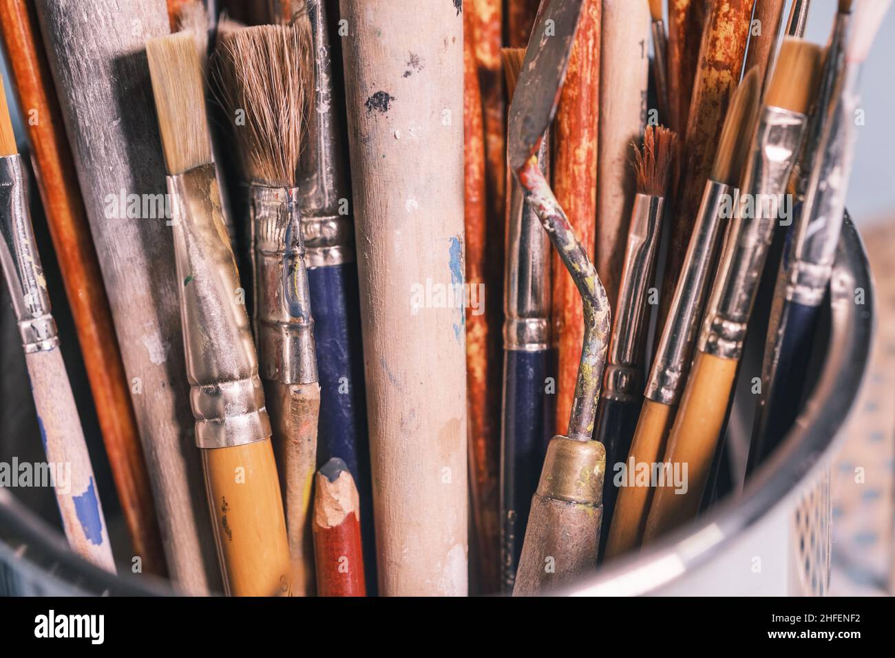 A bunch of well used painter's brushes with wooden handle in a metal bucket. Creative background Stock Photo
