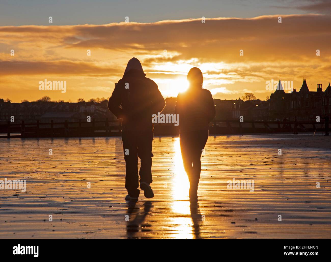 Portobello, Edinburgh, Scotland, UK. 16th January 2022. Finally sunrise sunshine with temperature of 7 degrees after a week of heavy cloud in the skies above the city. Pictured: A young couple take a dawn stroll along the sandy beach at the seaside. Credit: Scottishcreative/Alamy Live News. Stock Photo