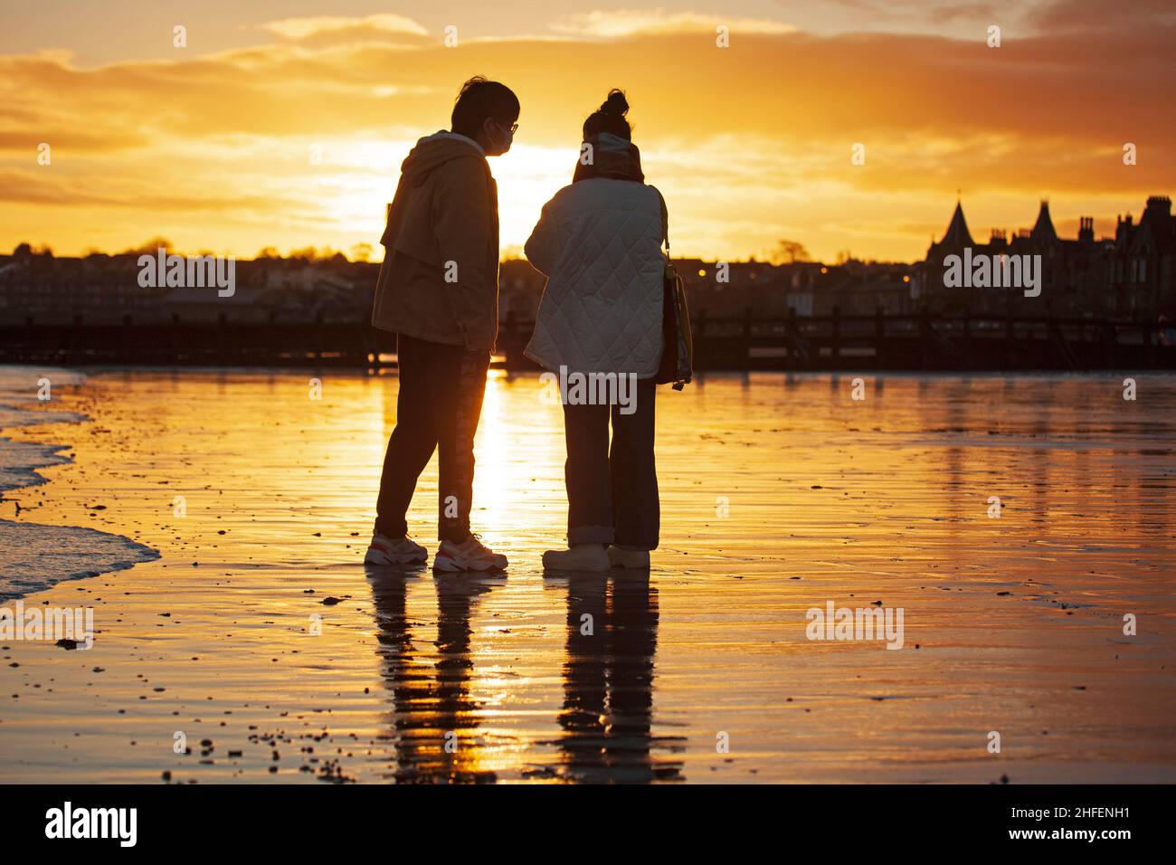 Portobello, Edinburgh, Scotland, UK. 16th January 2022. Finally sunrise sunshine with temperature of 7 degrees after a week of heavy cloud in the skies above the city. Pictured: Asian tourists enjoy the calm atmosphere at the seaside. Credit: Scottishcreative/Alamy Live News. Stock Photo