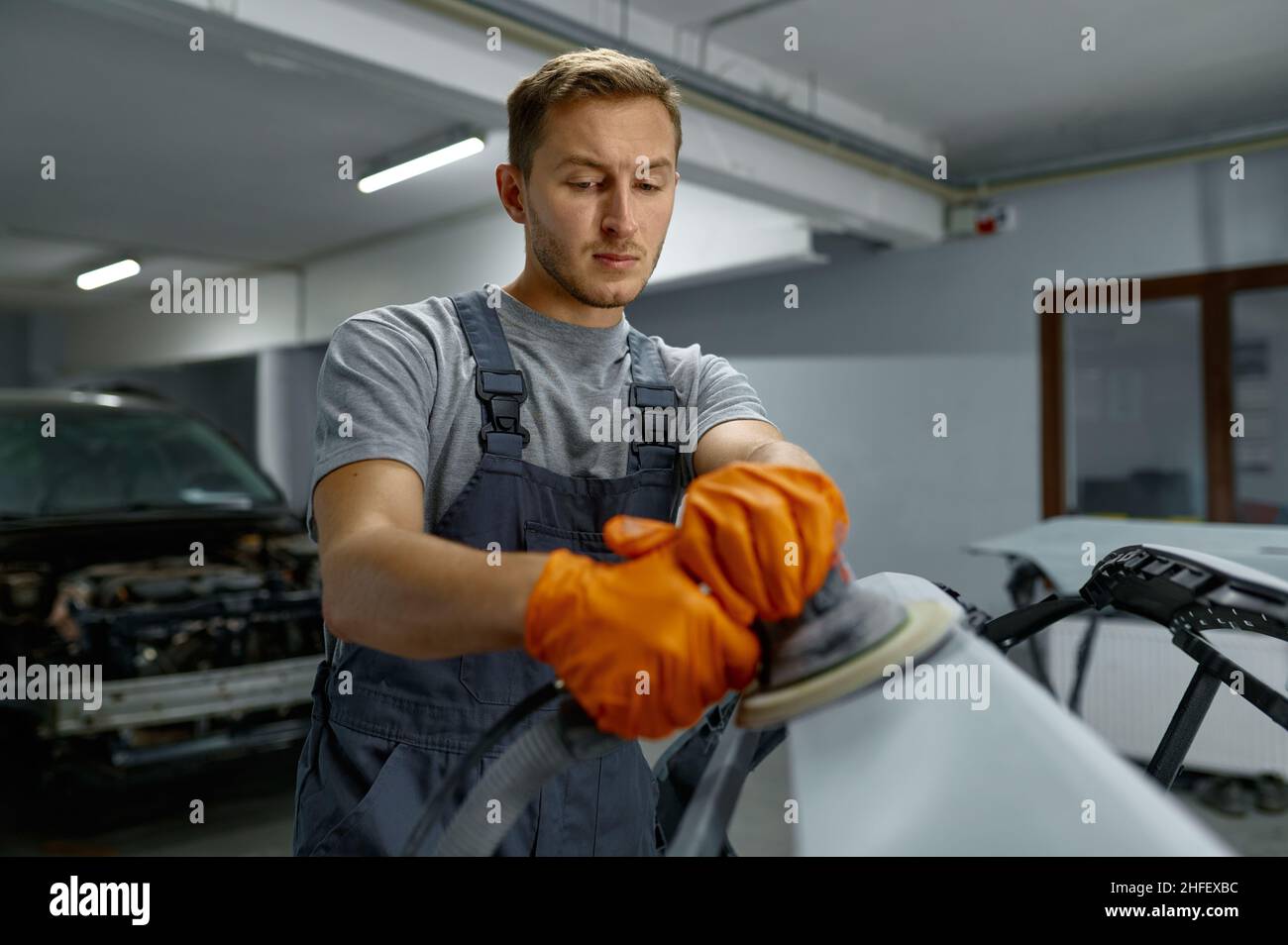 Serviceman polishing car body part in workshop Stock Photo