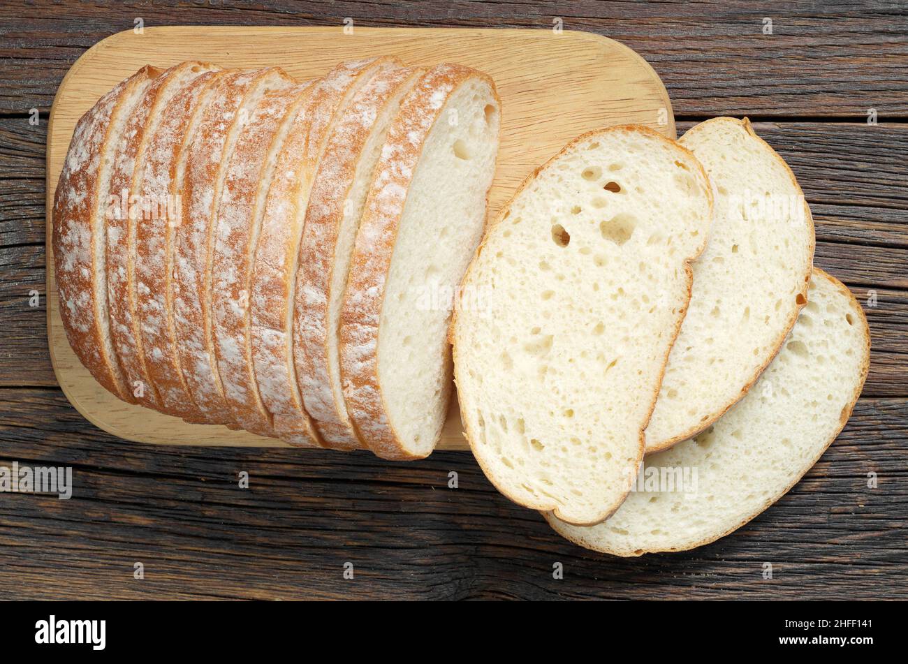 Sliced wheat bread on cutting board is located on an old wooden table ...