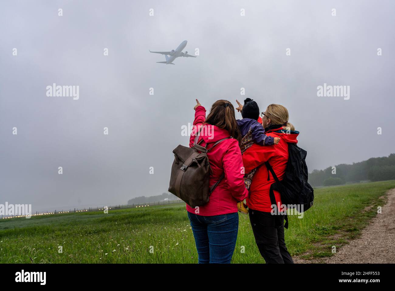 Two women with a child in their arms watch airplanes Stock Photo