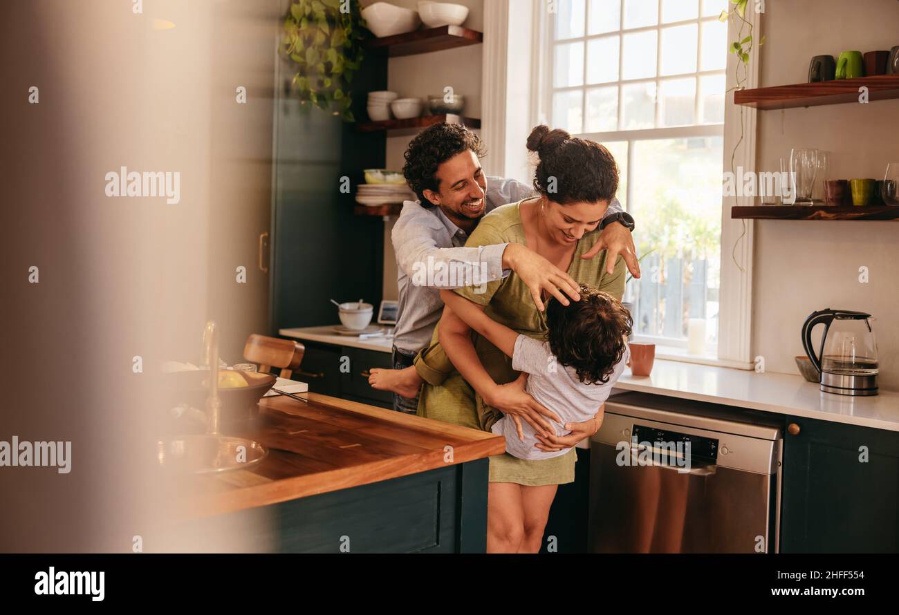 Parents playing with their son in the kitchen. Two happy parents laughing and having fun with their young son at home. Family of three spending some q Stock Photo