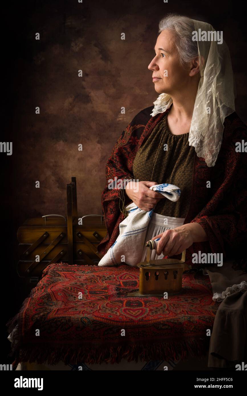 Old woman in victorian dress working with an antique charcoal iron on a board Stock Photo