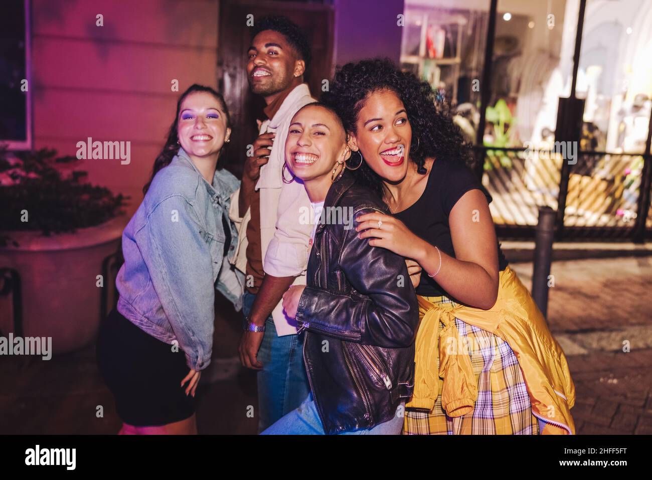 City friends having a good time outdoors. Group of multicultural young people smiling happily while standing together at night. Cheerful friends hangi Stock Photo