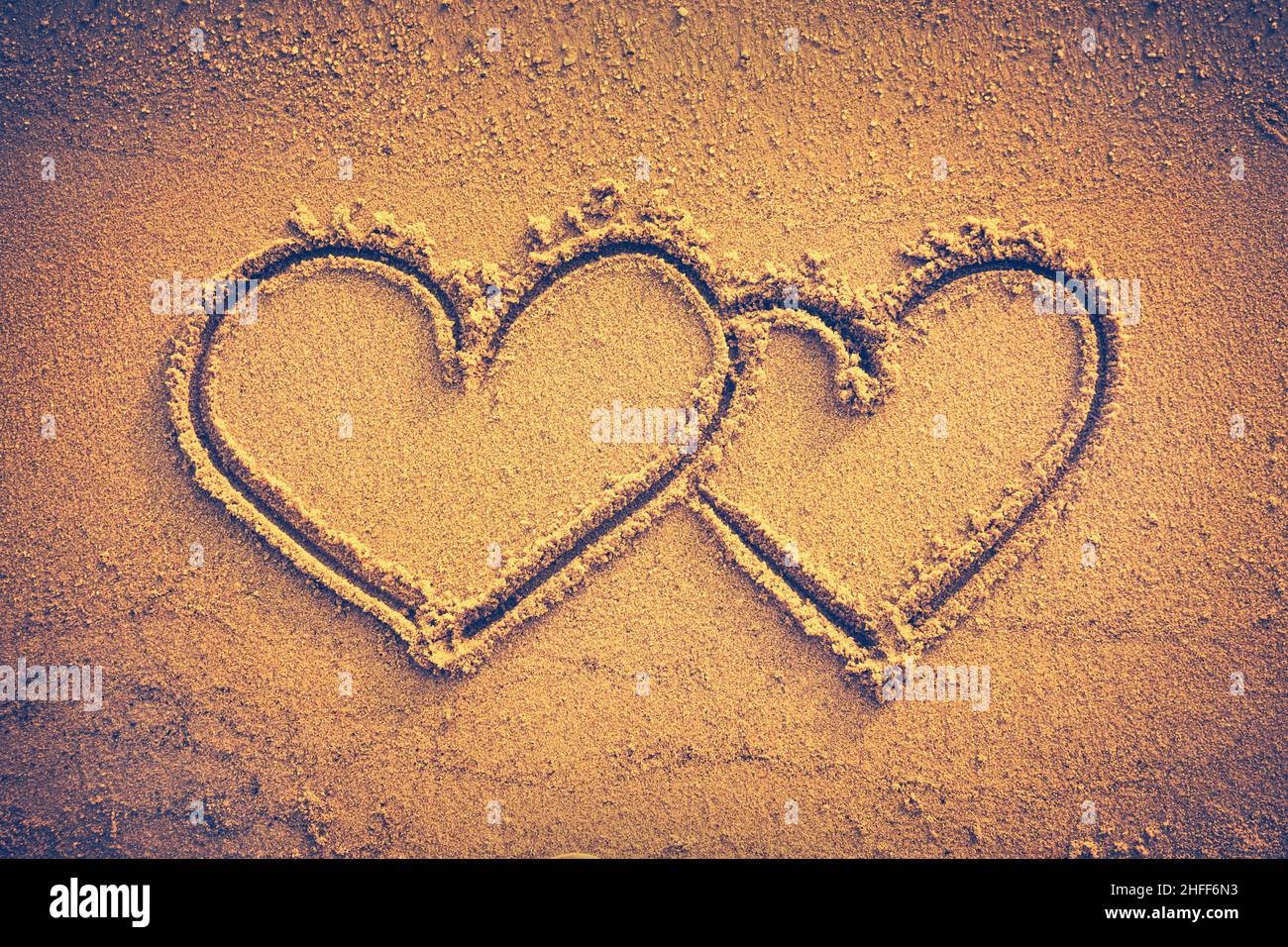 Two hearts handwritten on seashore sand. Valentine's day on the beach. Vignette and vintage picture style. Warm tone. Stock Photo