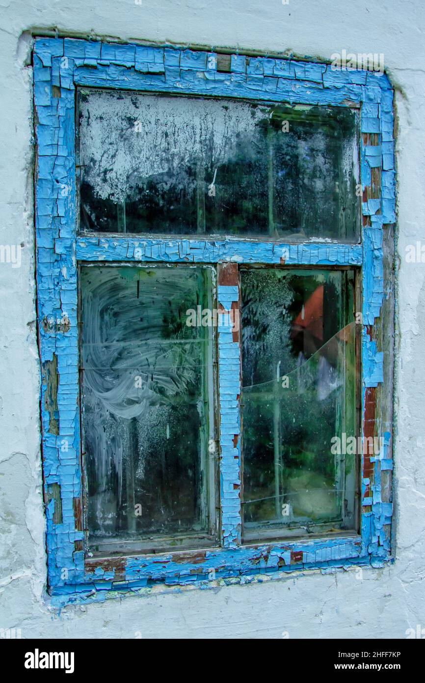 View of old abandoned house window with broken glass and peeled blue ...
