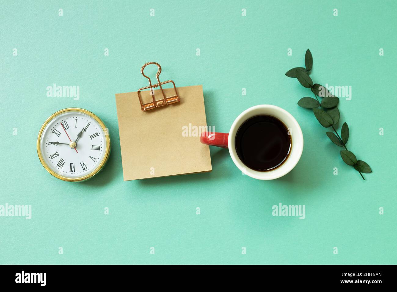 Notepad, clock, cup of coffee, green leaf on mint green background. office desk, workspace. top view Stock Photo