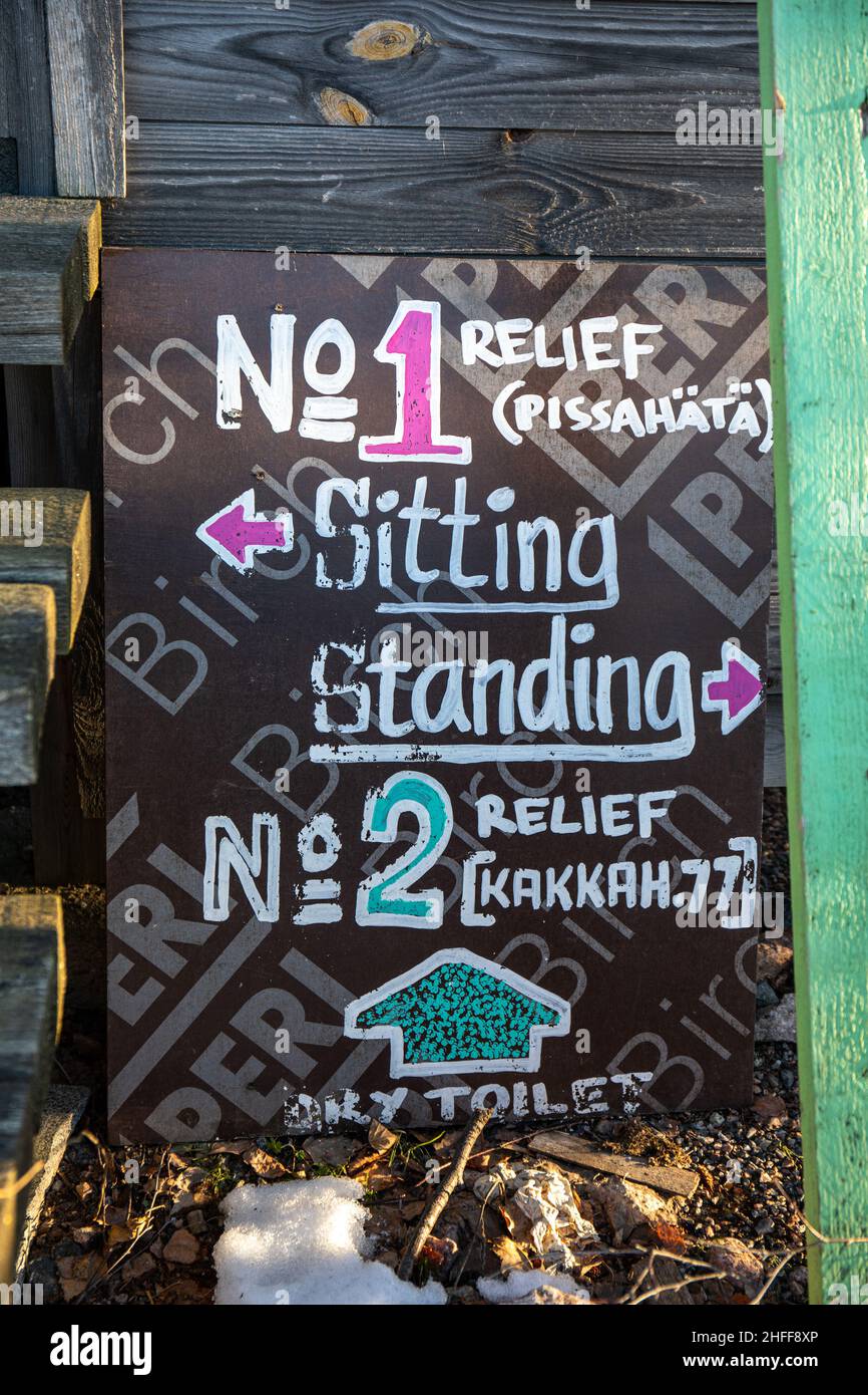 Relief options. Sitting and standing pissoirs and dry toilet. Hand written sign against wooden outdoor toilet in Helsinki, Finland. Stock Photo
