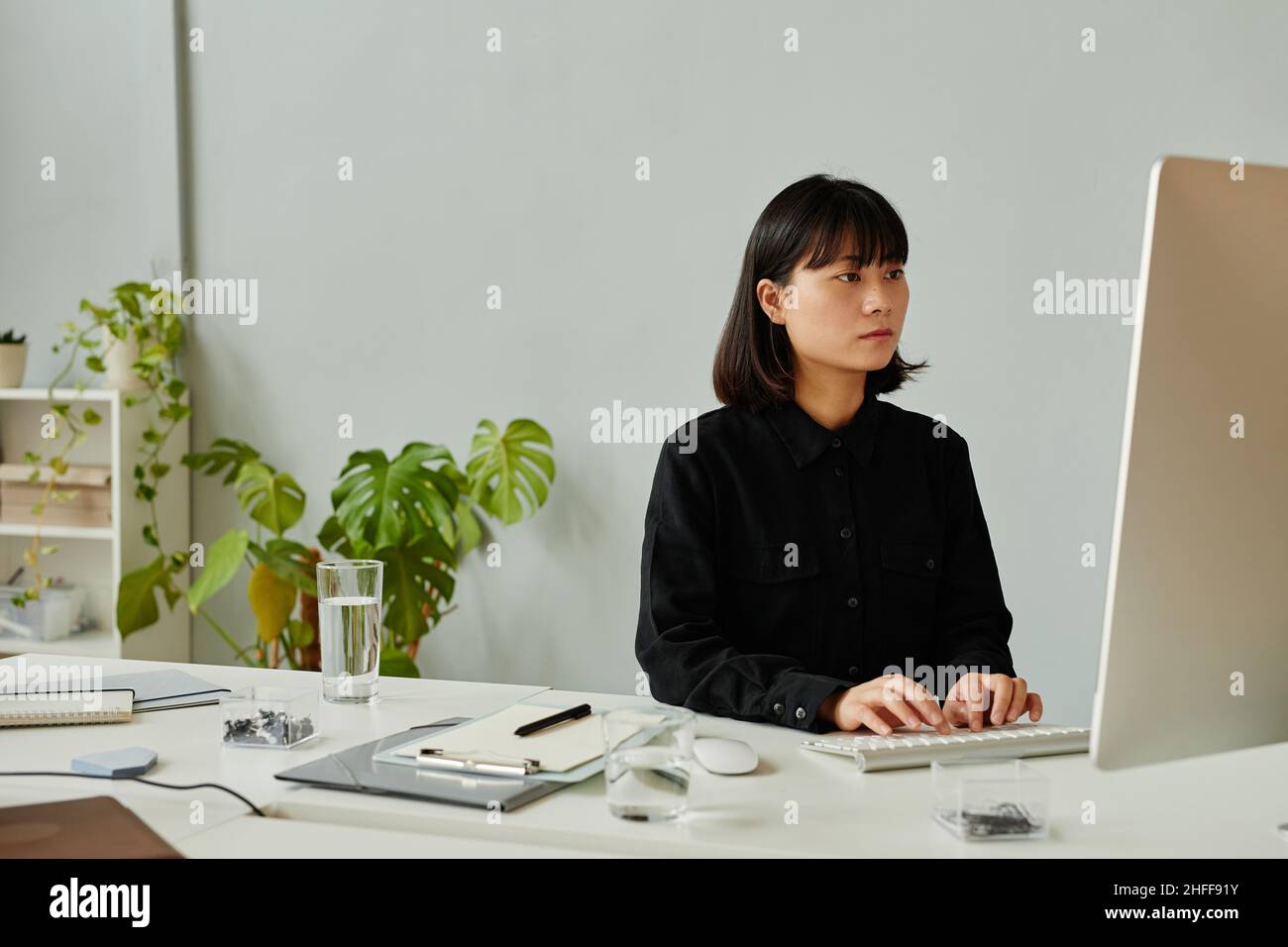 Minimal portrait of young Asian woman using computers in modern office, copy space Stock Photo