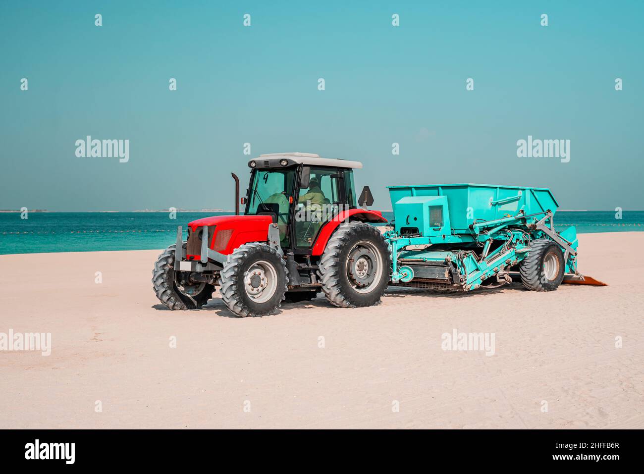 Red tractor on the sandy beach cleaning, excavator working on sand ...