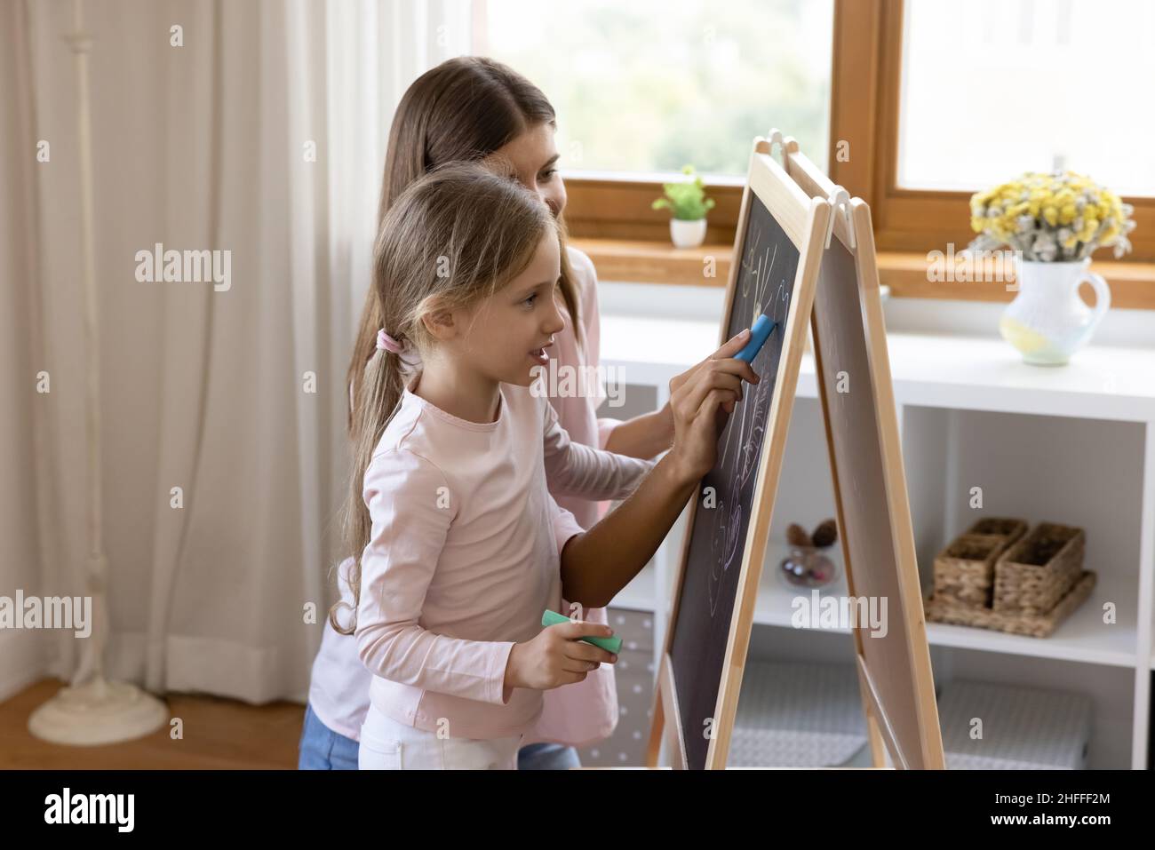 Mother and little daughter holding chalks drawing on board Stock Photo