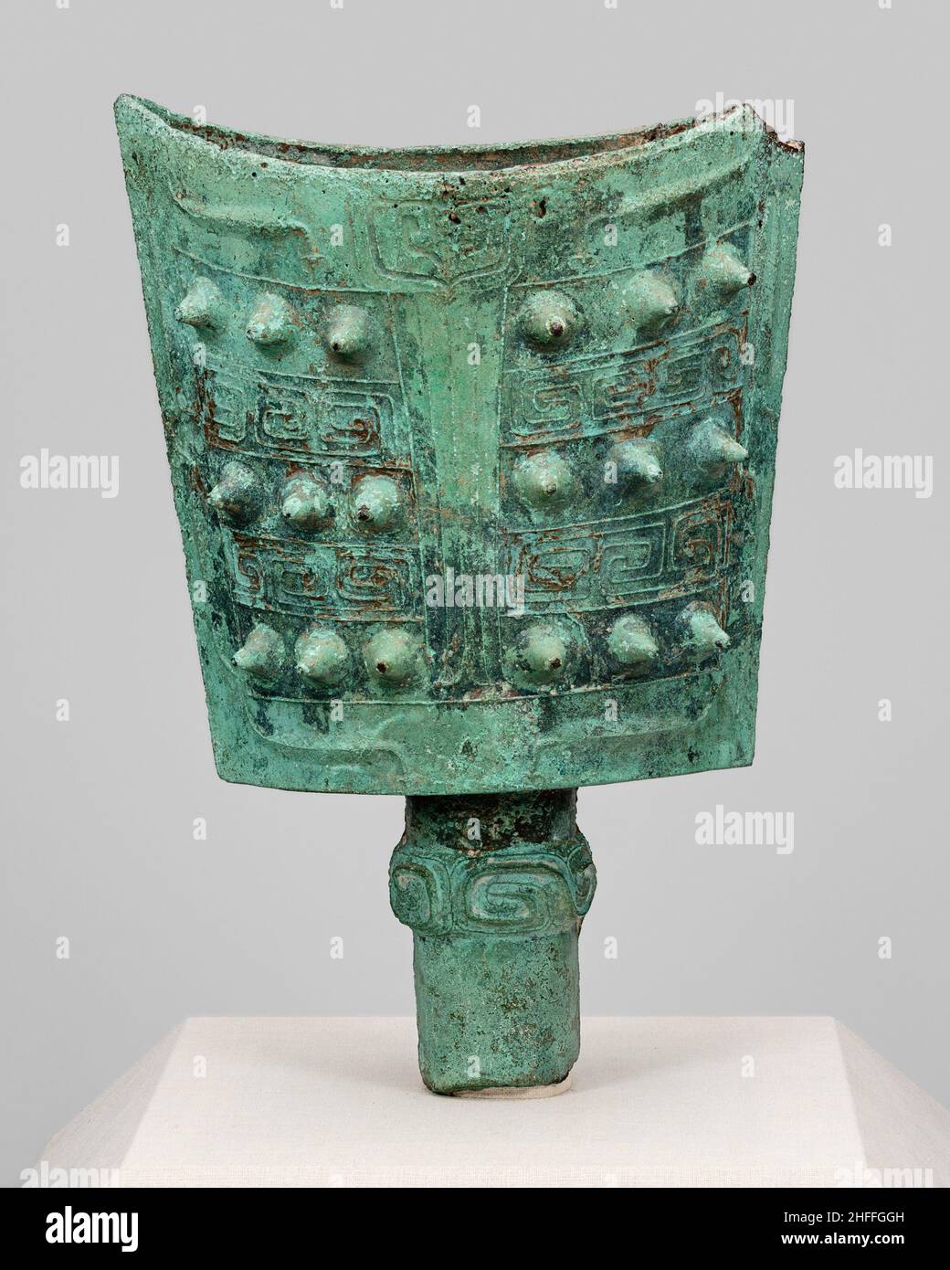 Bell (nao), Western Zhou dynasty (1046-771 B.C.). A bell with two convex sides of nearly rectangular shape and an opening at top rests on a slim cylindrical base. It boasts a green patina and is decorated with a geometric pattern and spikes. A small portion is missing at upper right. Stock Photo
