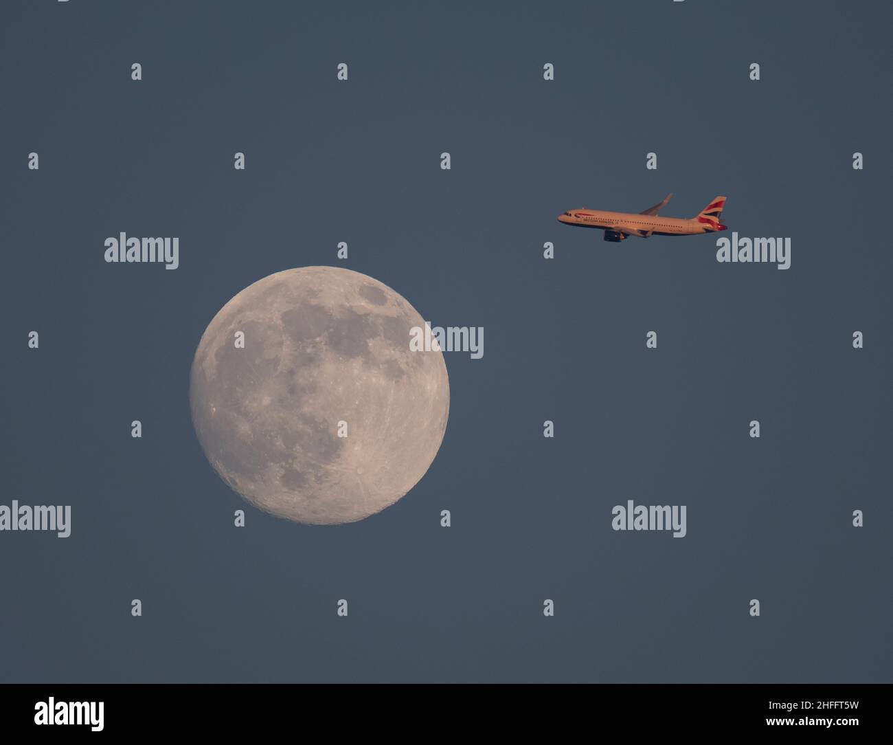 London, UK. 16 January 2022. Early evening British Airways flight from Tenerife on approach to London Heathrow and bathed in setting sunlight passes the almost full Moon over London. Credit: Malcolm Park/Alamy Live News Stock Photo