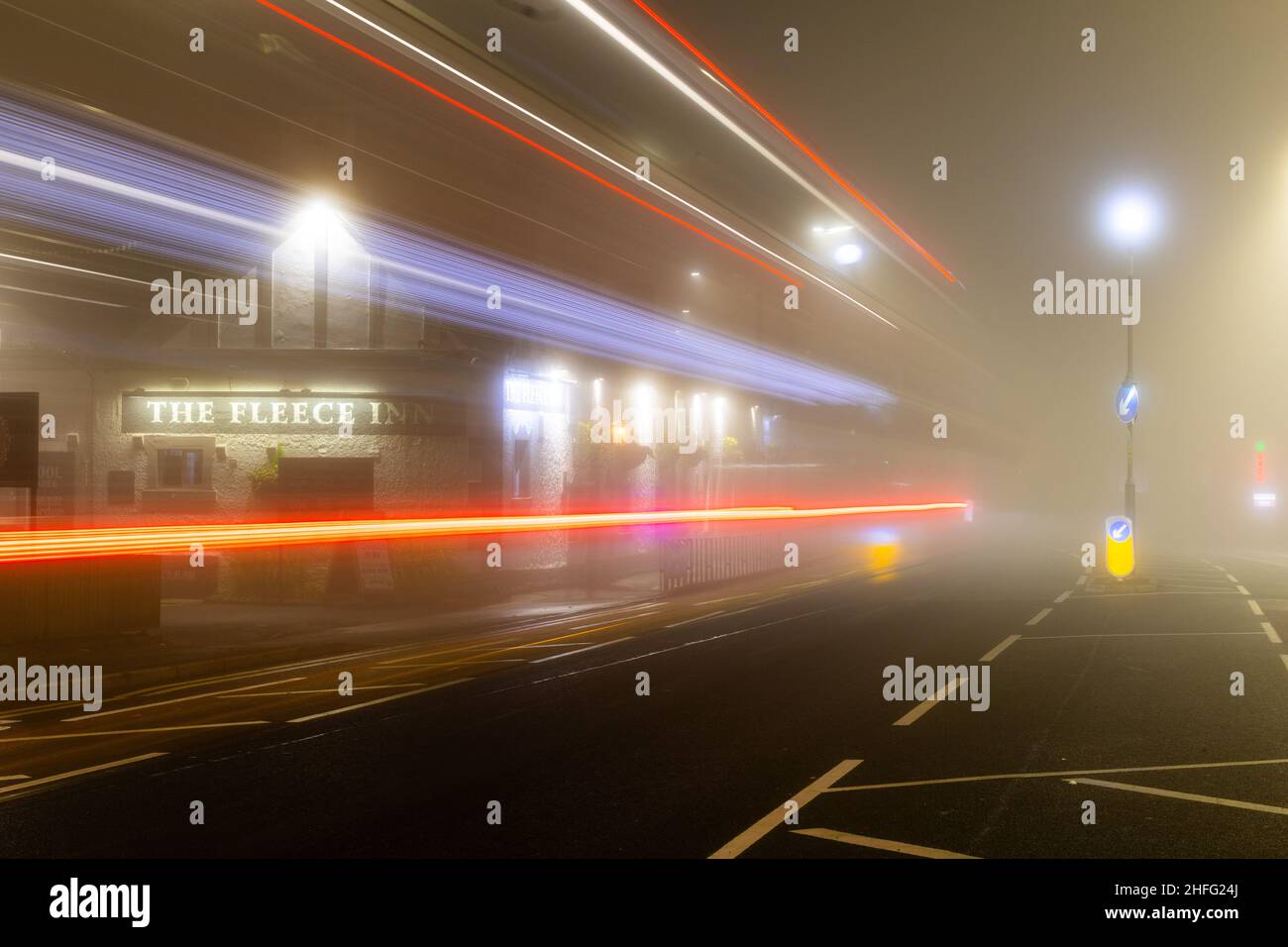 British pub, The Fleece Inn, shot in morning fog showing light streaks of passing cars. Stock Photo
