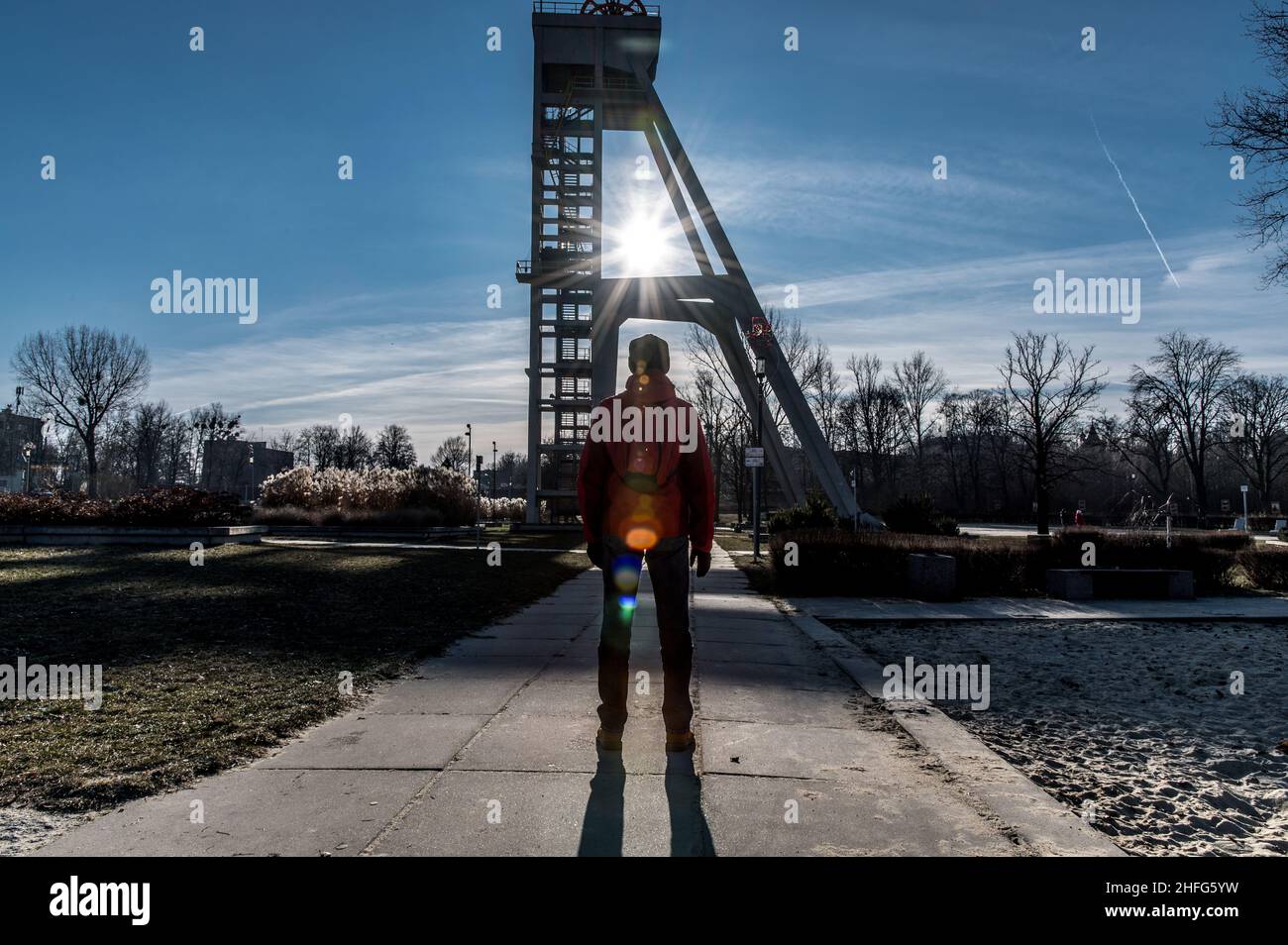 A man in a red winter jacket watching the sun rays through the structure of a mine shaft in the Silesia landscape Stock Photo