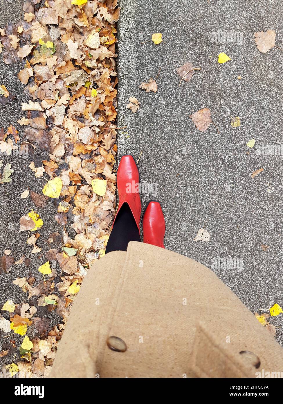 Legs seen from above with red shoes walking on yellow leaves in Autumn Stock Photo