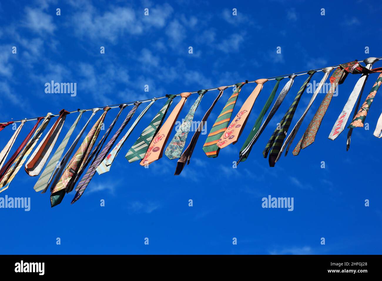 Viele bunte Krawatten hängen an einer Wäscheleine, blauer Himmel  /  Many colorful ties hanging on a clothesline, blue sky Stock Photo
