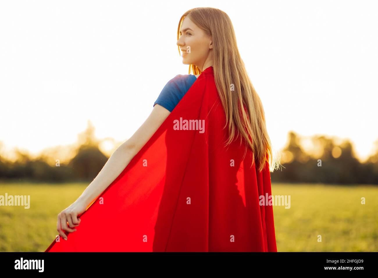 Photo from the back Woman superhero. blonde in the image of a superheroine  in a red cloak is growing up. Joyful beautiful woman in superhero costume p  Stock Photo - Alamy