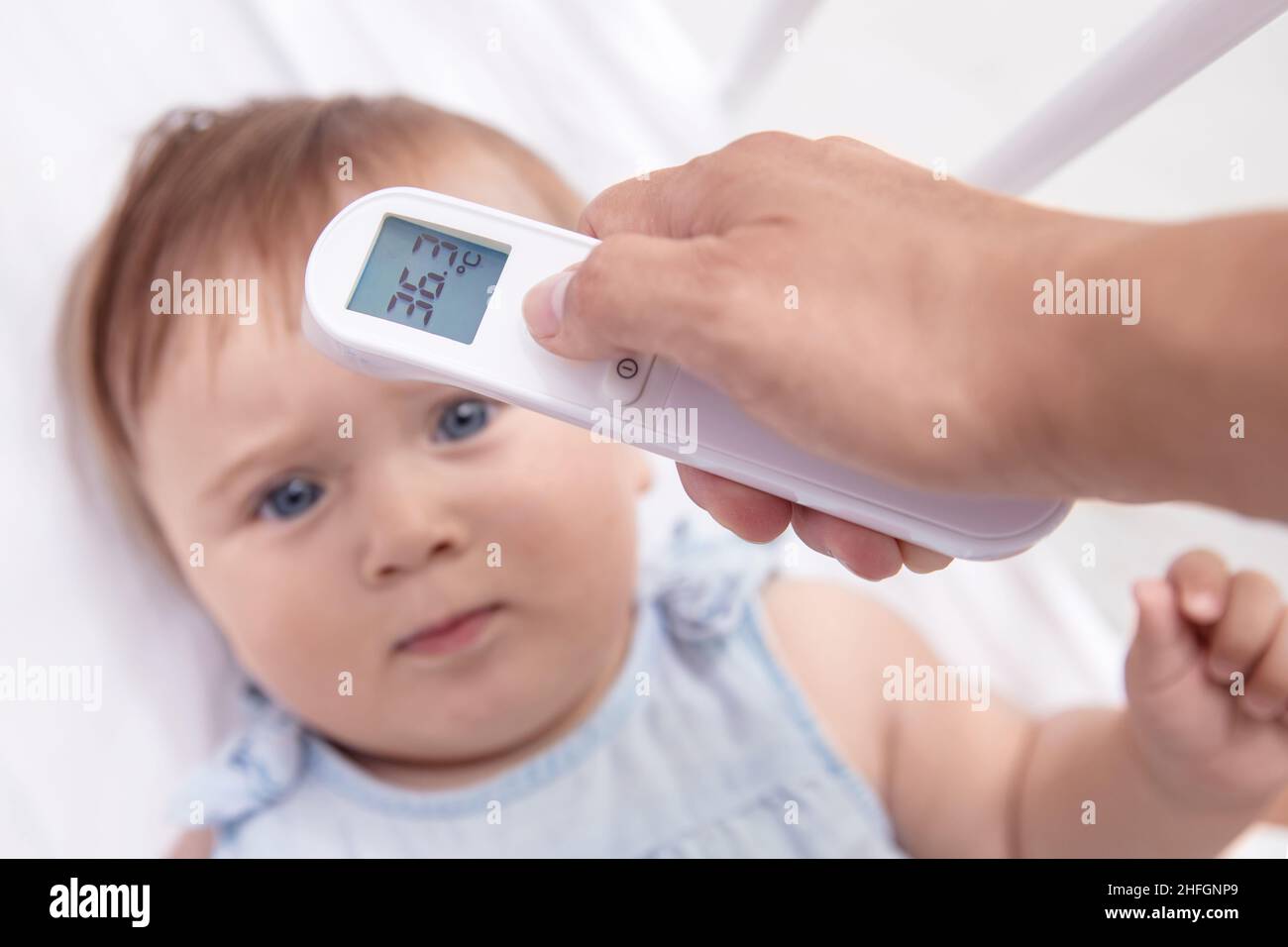 Mother checks baby's  temperature with modern electronic termomether at baby's forehead Stock Photo
