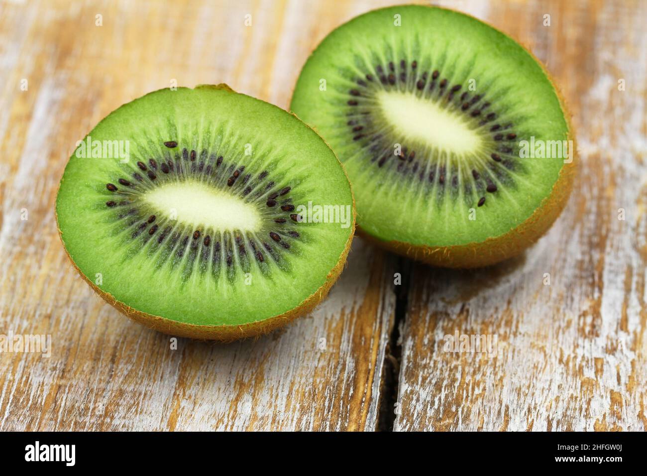 Closeup of two halves of juicy fresh kiwi fruit on rustic wooden surface Stock Photo