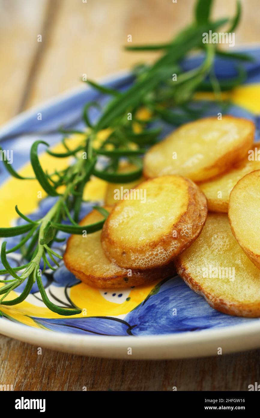 Slices of fried potatoes and fresh rosemary on vintage plate Stock Photo