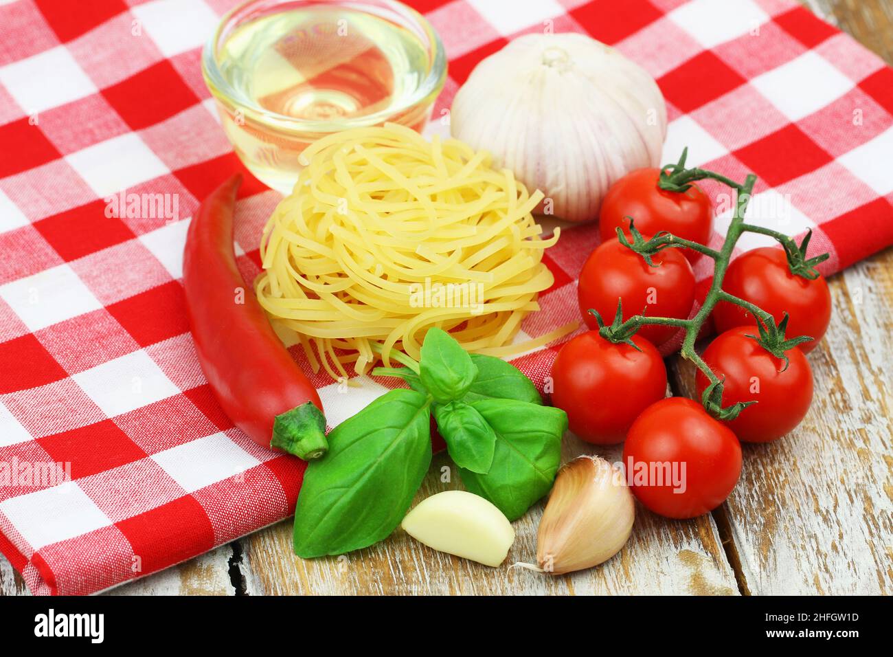 Ingredients for cooking pasta: tagliatelle, cherry tomatoes, garlic, fresh basil, chili and bowl of olive oil Stock Photo