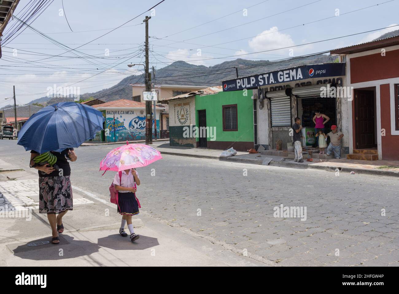 A woman and a girl walk with parasols to shade them from bright tropical sun in Jinotega, Nicaragua. Stock Photo